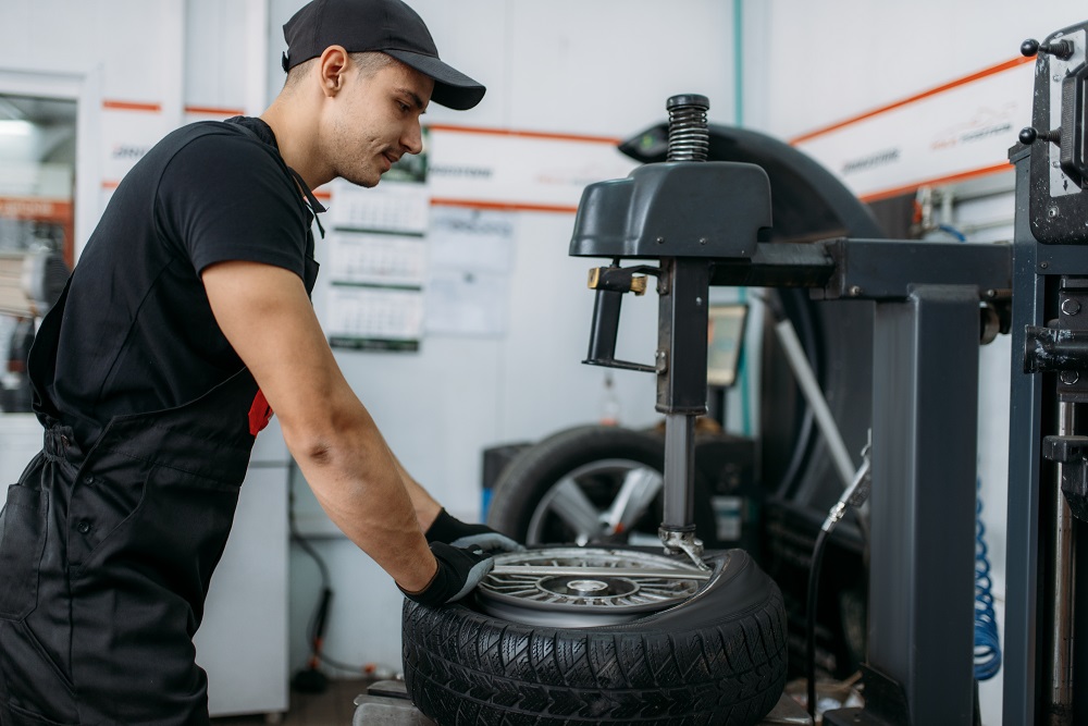 Mechanic fixing broken wheel on tire fitting machine, repairing service. Man repairs car tyre in garage, automobile inspection in workshop